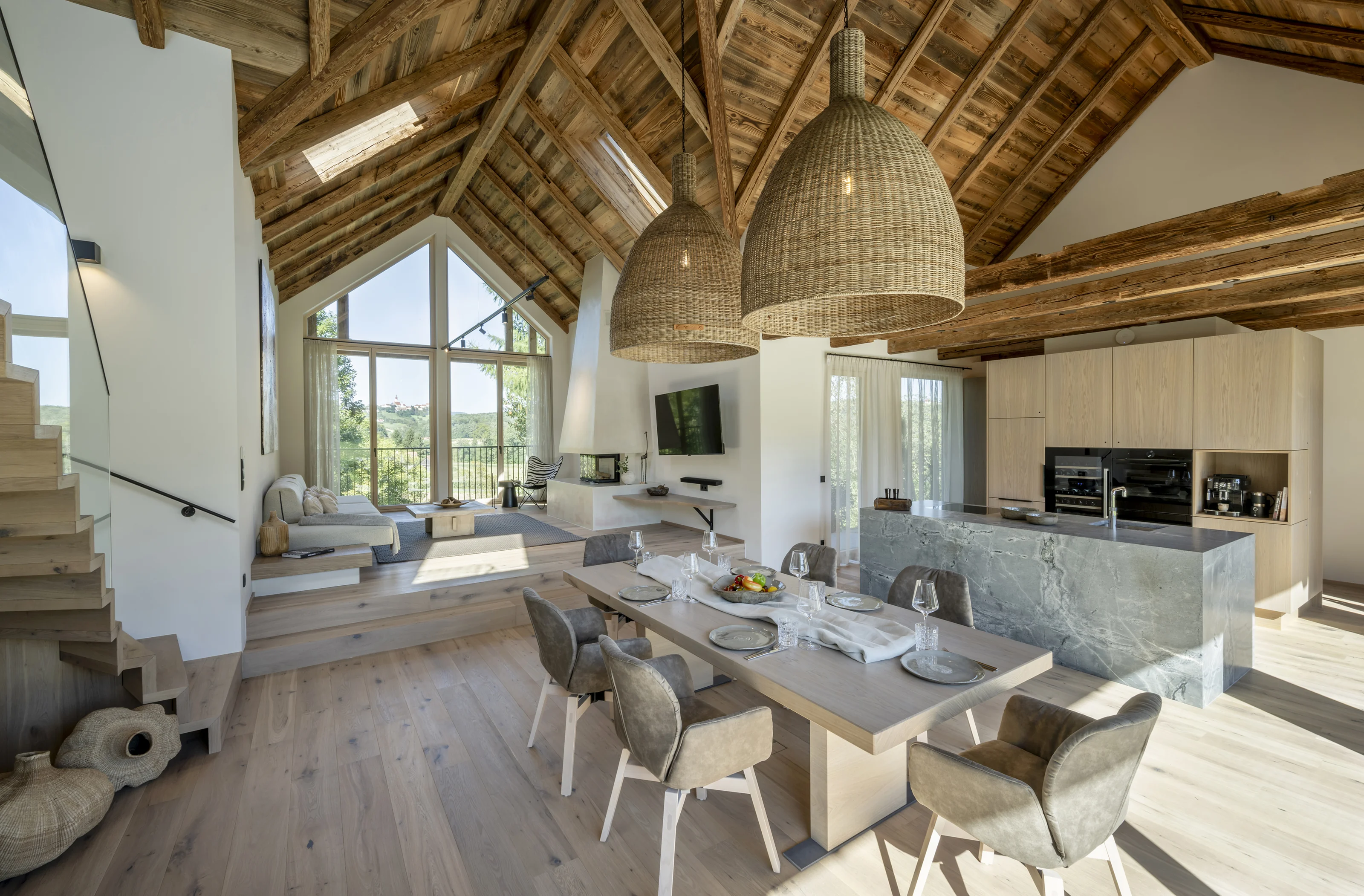 Offener Wohn- und Essbereich im Julianhof mit sichtbarem Holzdach, Natursteininsel und großen Fenstern.