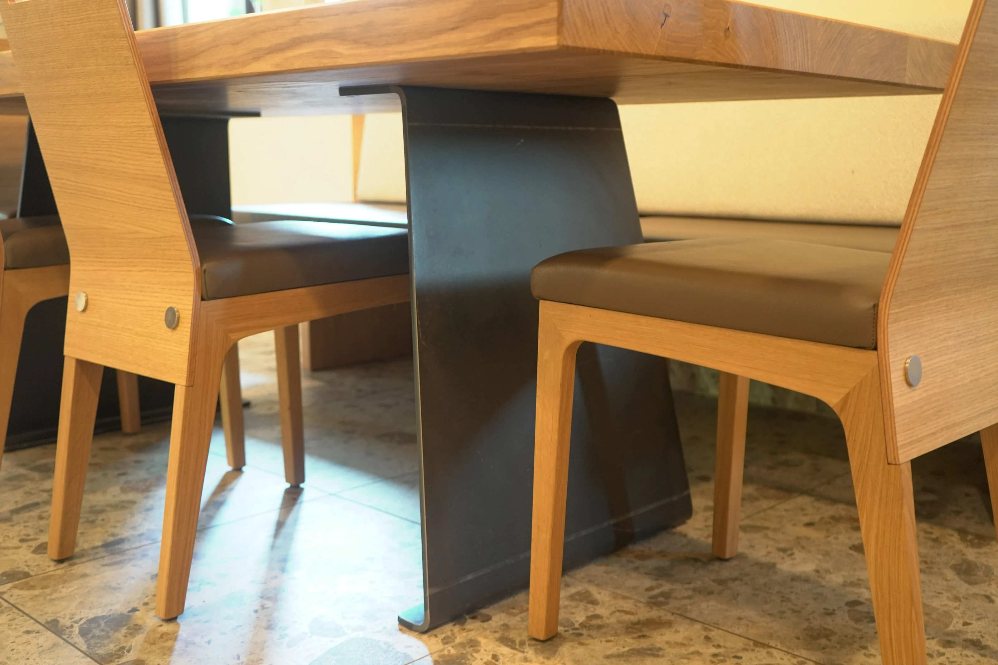 Holztisch mit dunklem Mittelgestell und gepolsterten Holzstühlen.