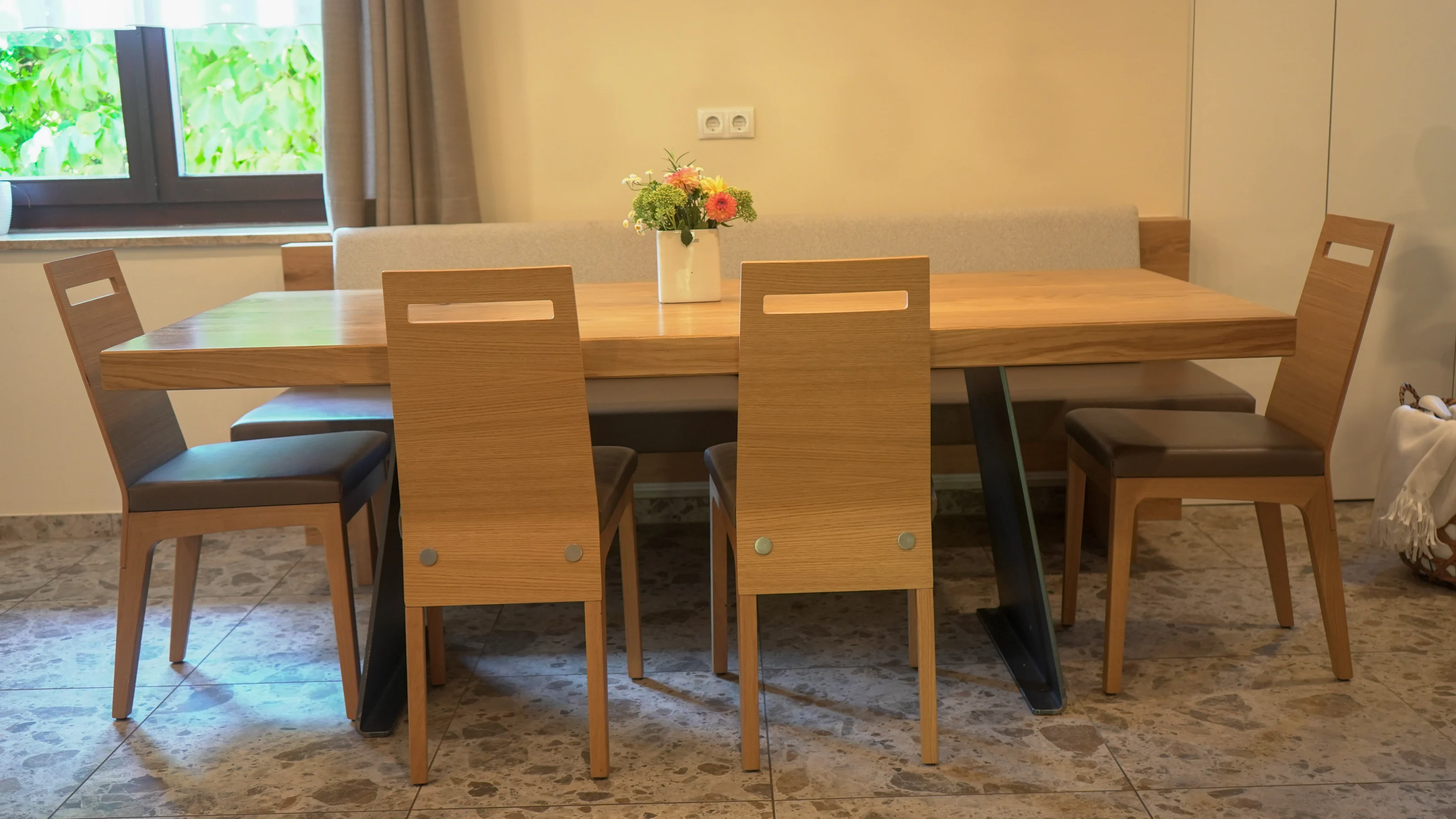 Essbereich mit Holztisch, Holzstühlen und gepolsterter Sitzbank am Fenster.